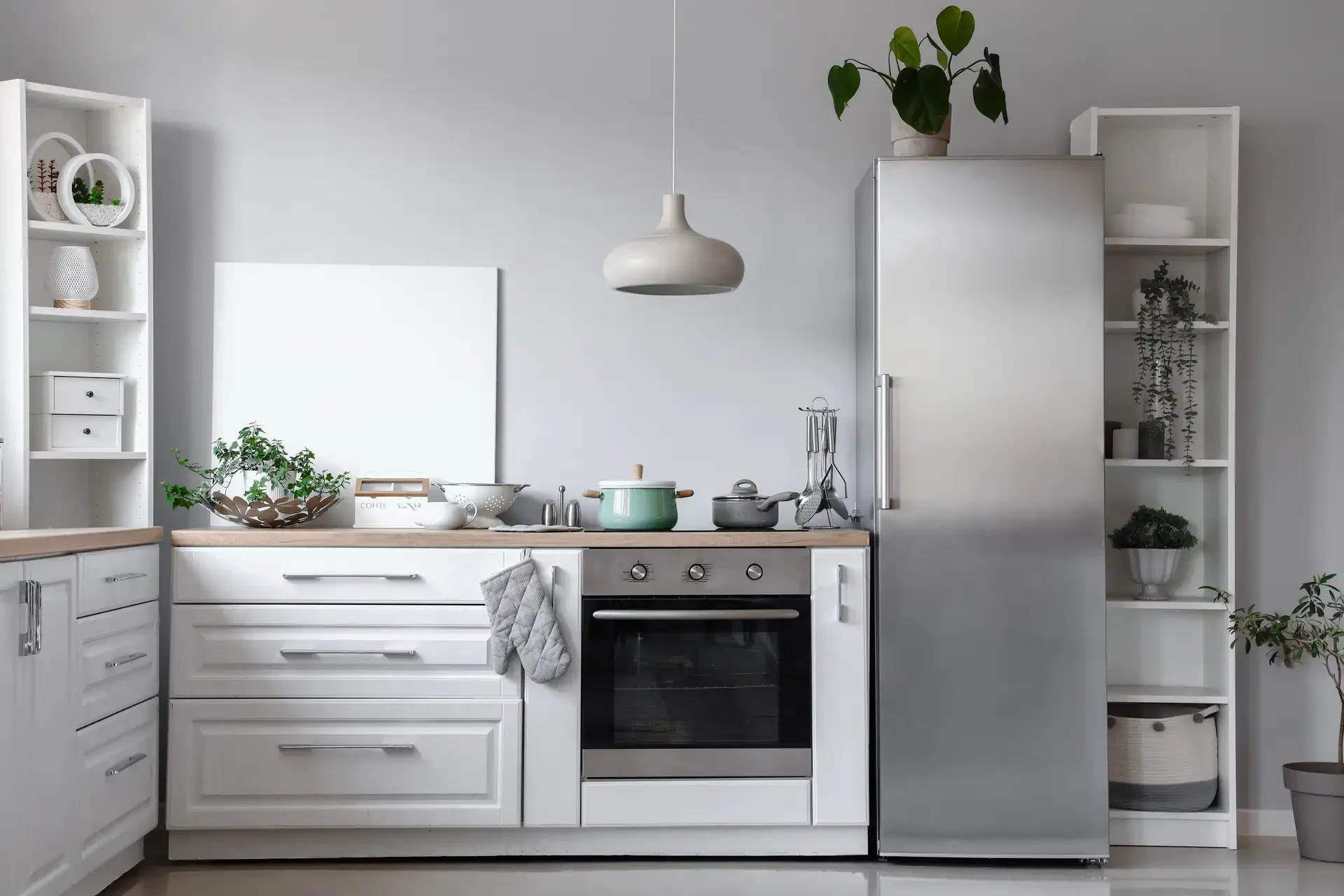 Stainless steel refrigerator with vertical handle in modern kitchen next to oven with organized cabinets and shelving
