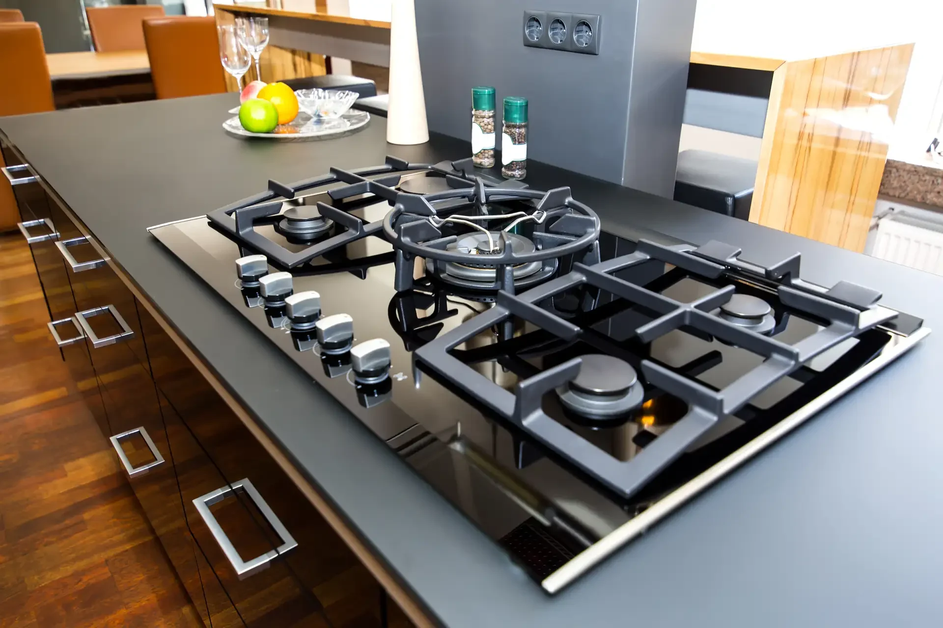 Modern built-in gas cooktop with black glass surface and cast iron grates installed in kitchen island