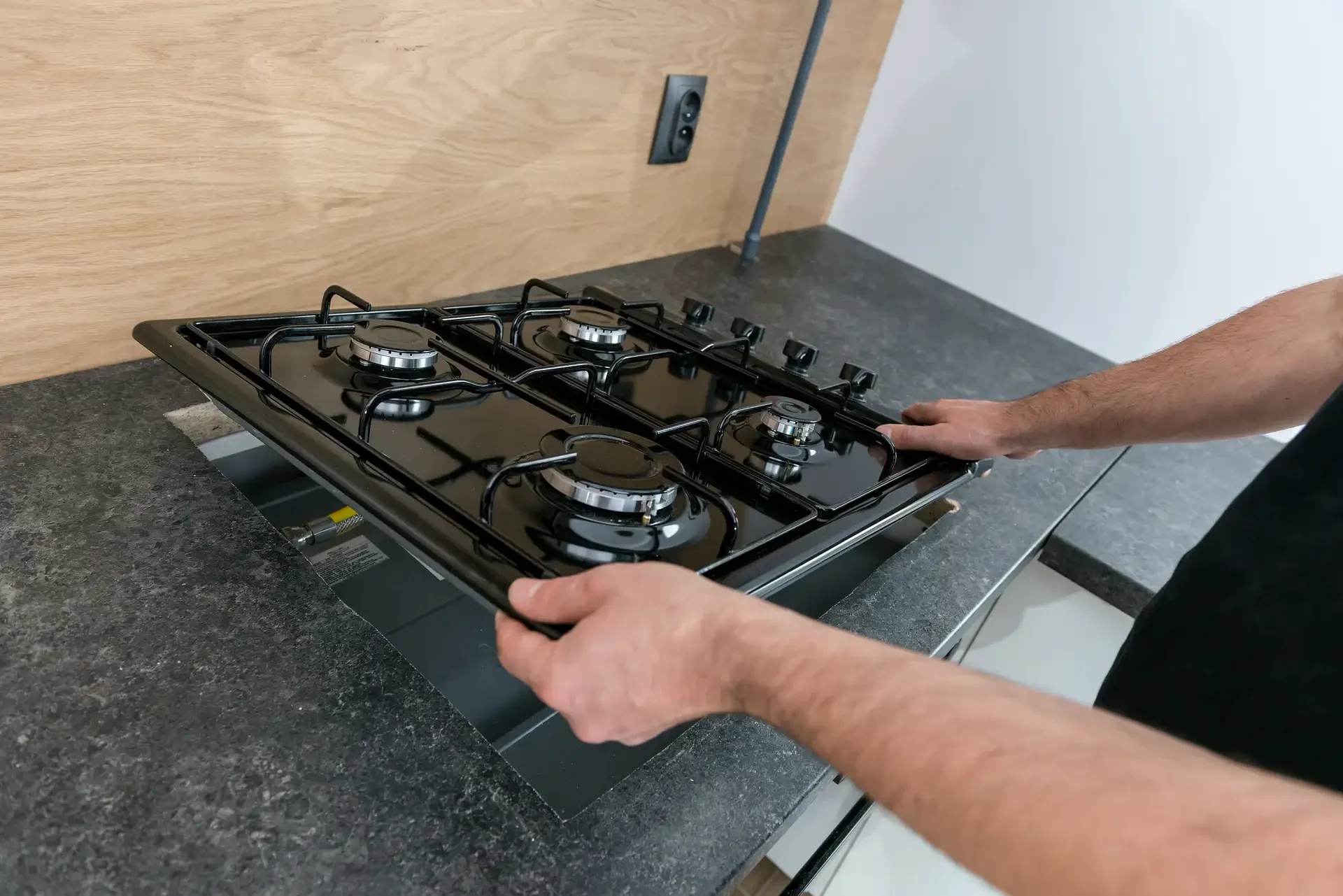 Technician lifting gas cooktop from countertop opening, exposing gas lines and connection points during appliance repair or installation