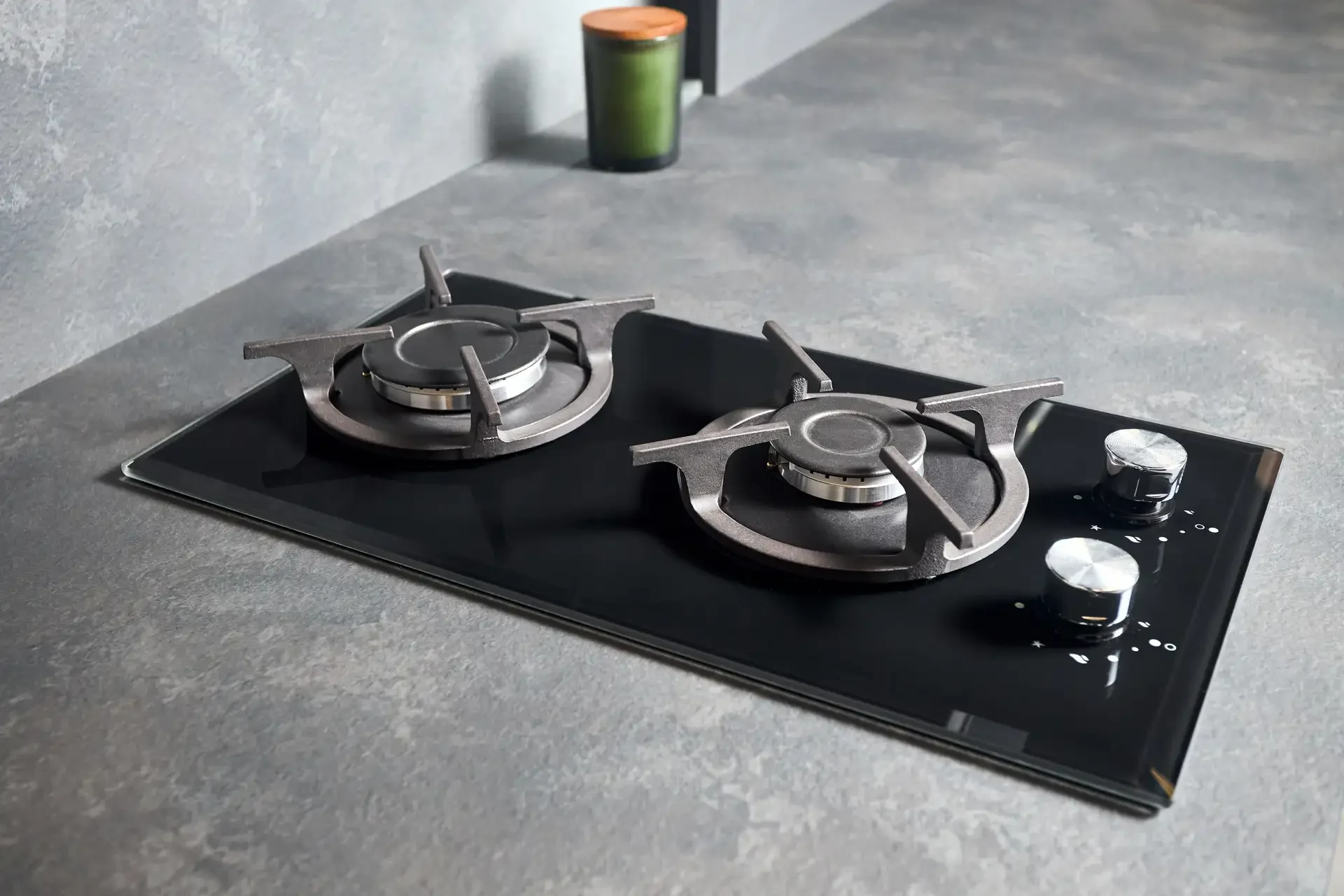 Modern two-burner gas cooktop with black glass surface and metallic control knobs installed on grey countertop