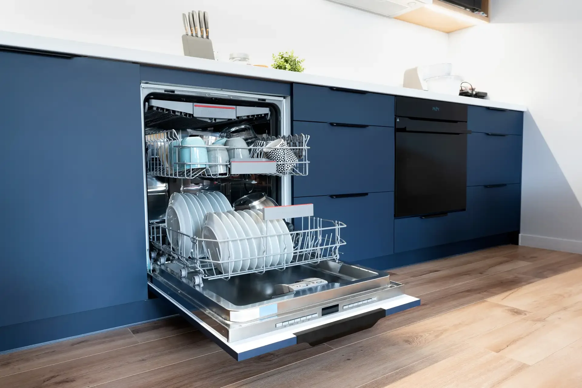 Open built-in dishwasher with loaded dish racks integrated into blue kitchen cabinets
