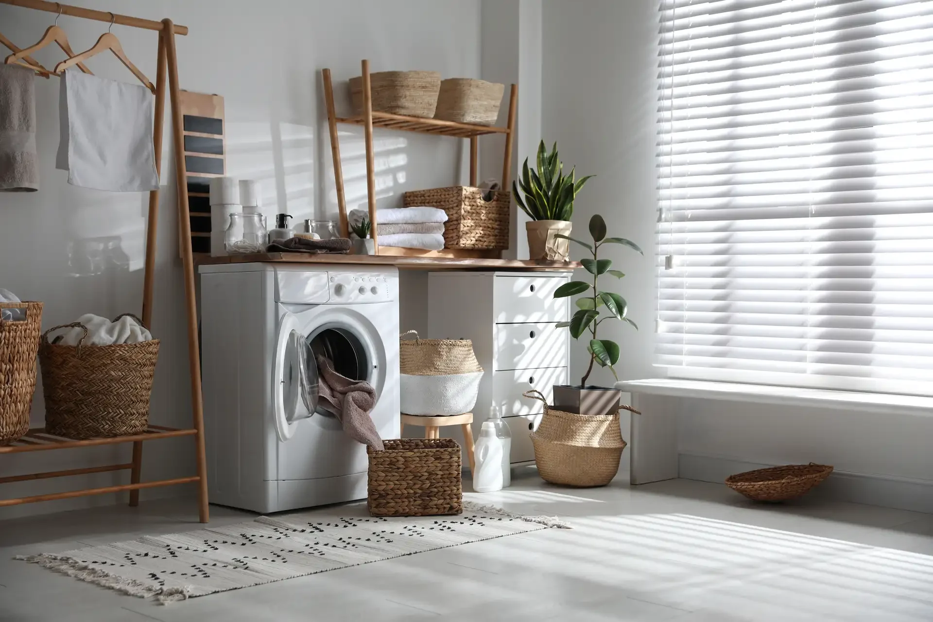 Front-loading washing machine with open door in organized laundry room with wicker baskets, towels, and natural lighting