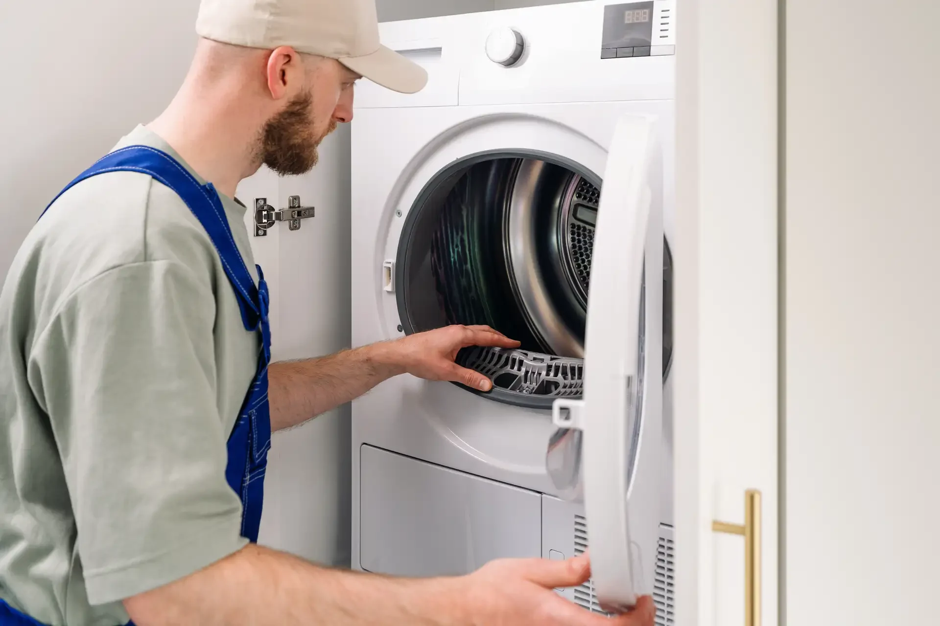 Appliance repair technician in uniform inspecting the interior of an open front-loading washing machine, handling internal components during service