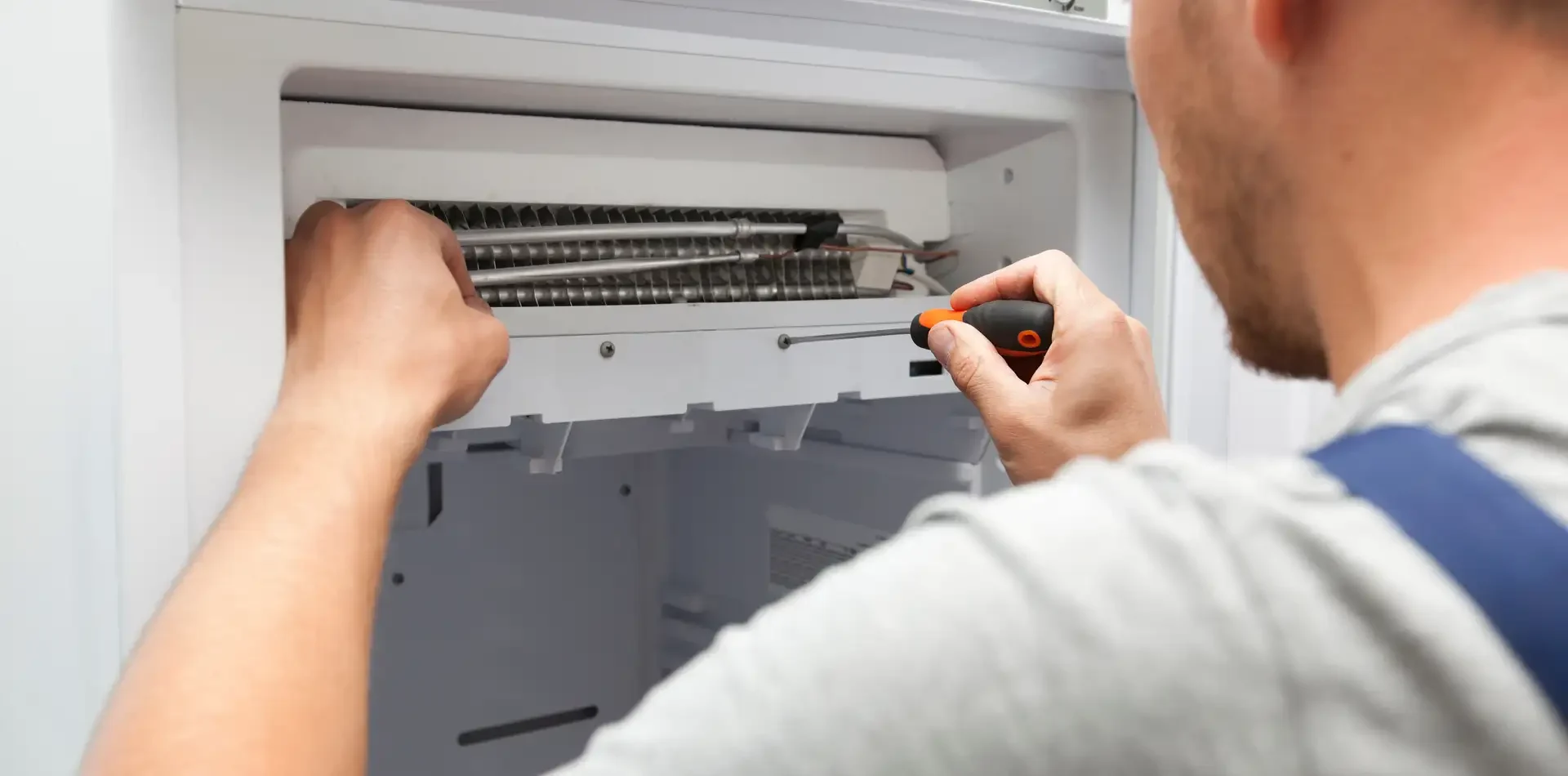 Refrigerator repair technician using screwdriver to work on internal evaporator coils with interior panel removed