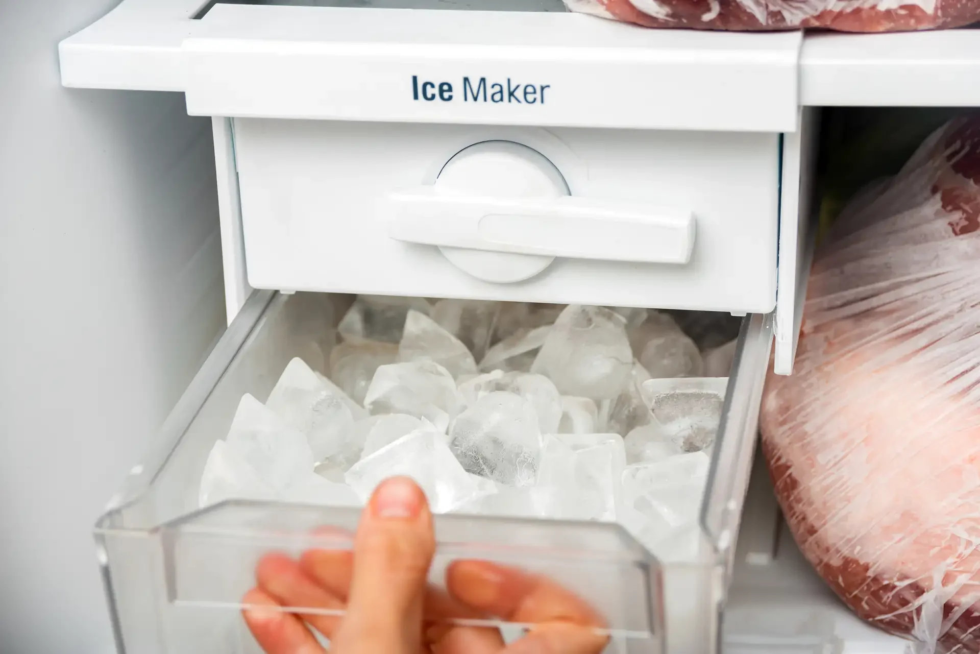 Hand pulling ice bin filled with clear ice cubes from refrigerator freezer compartment ice maker