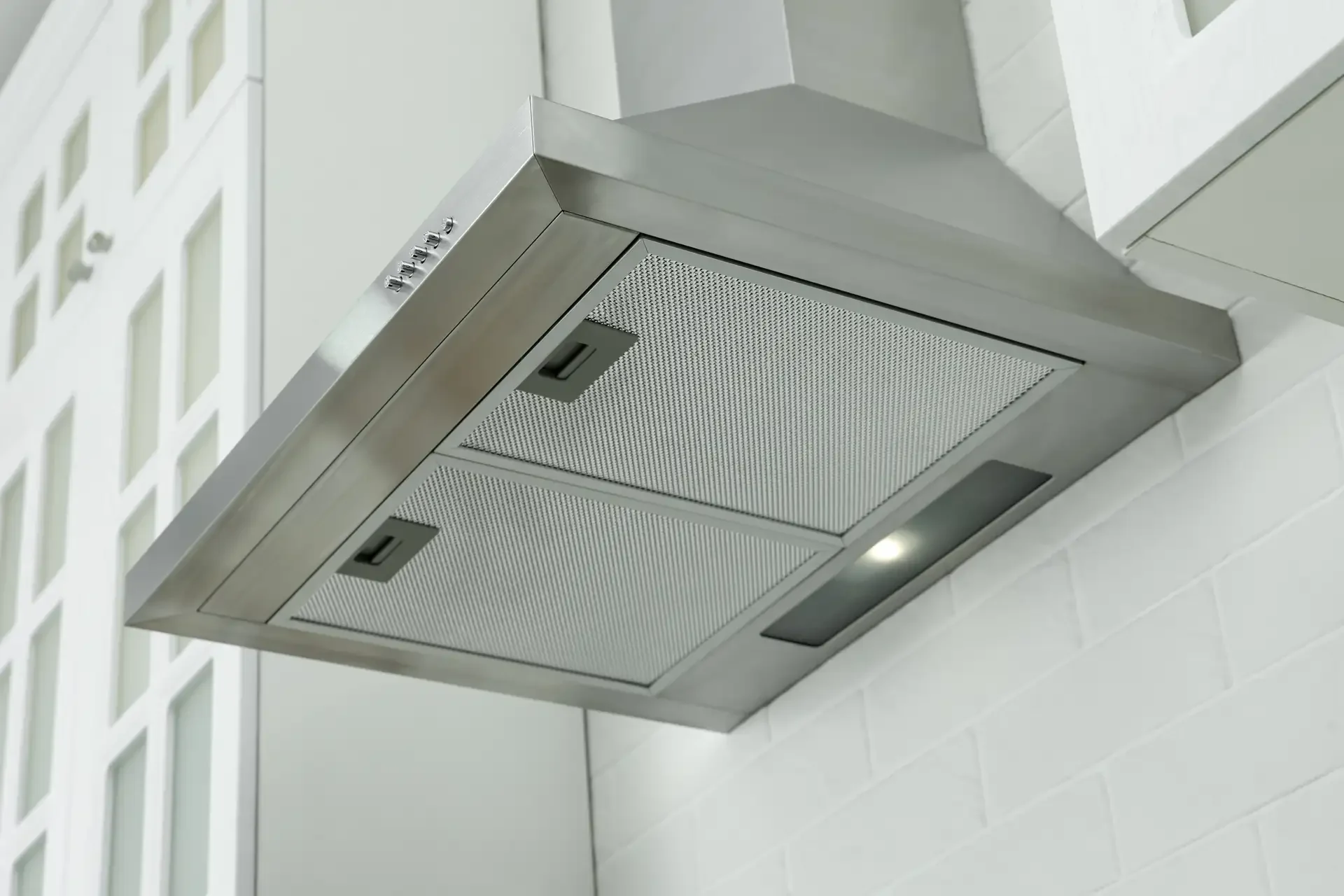 Modern stainless steel range hood with mesh filters and built-in lighting installed in clean kitchen setting