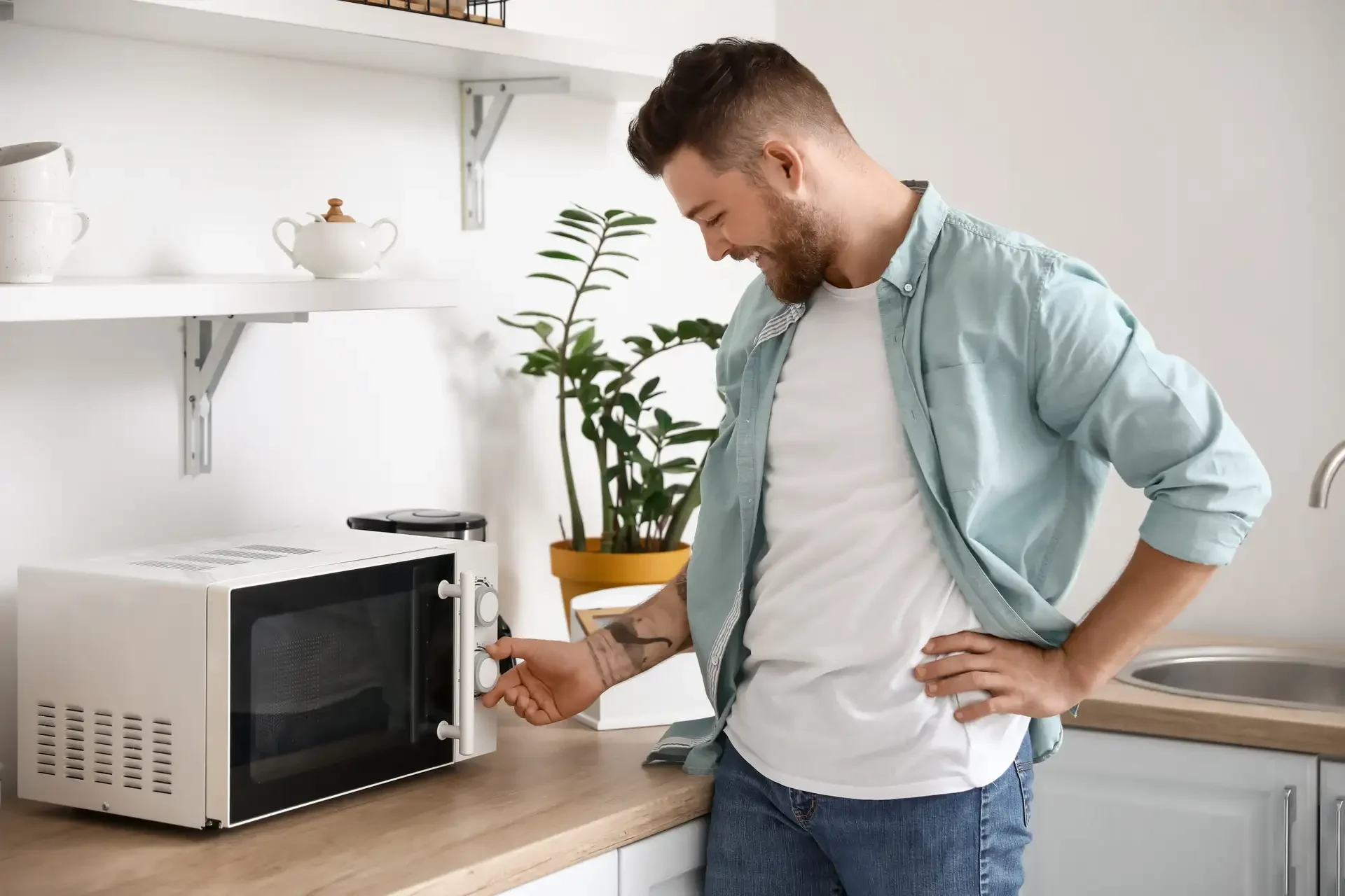 Man adjusting control knobs on a countertop microwave oven in a modern kitchen