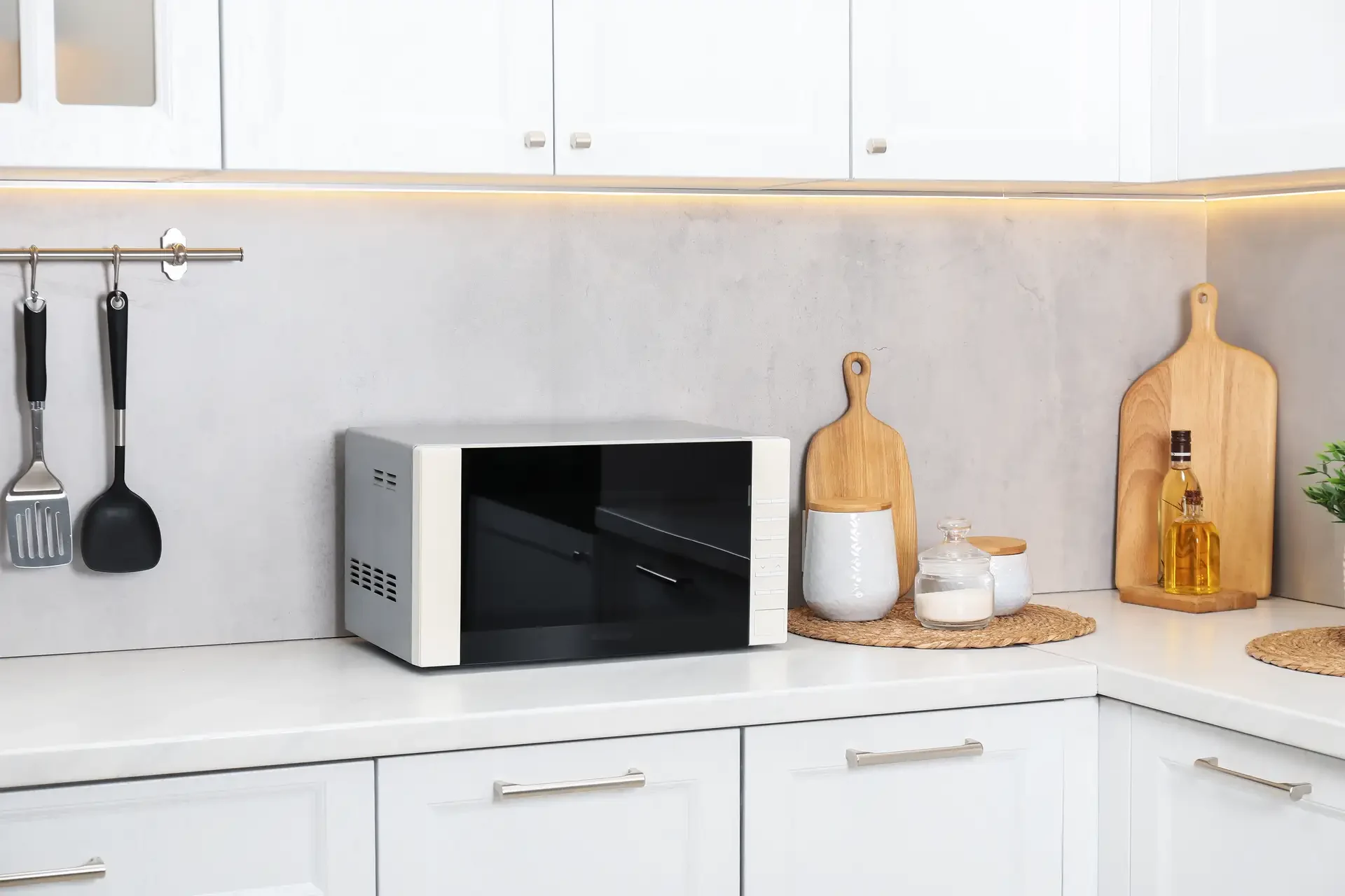 Modern microwave oven on white kitchen countertop surrounded by organized kitchen accessories and utensils