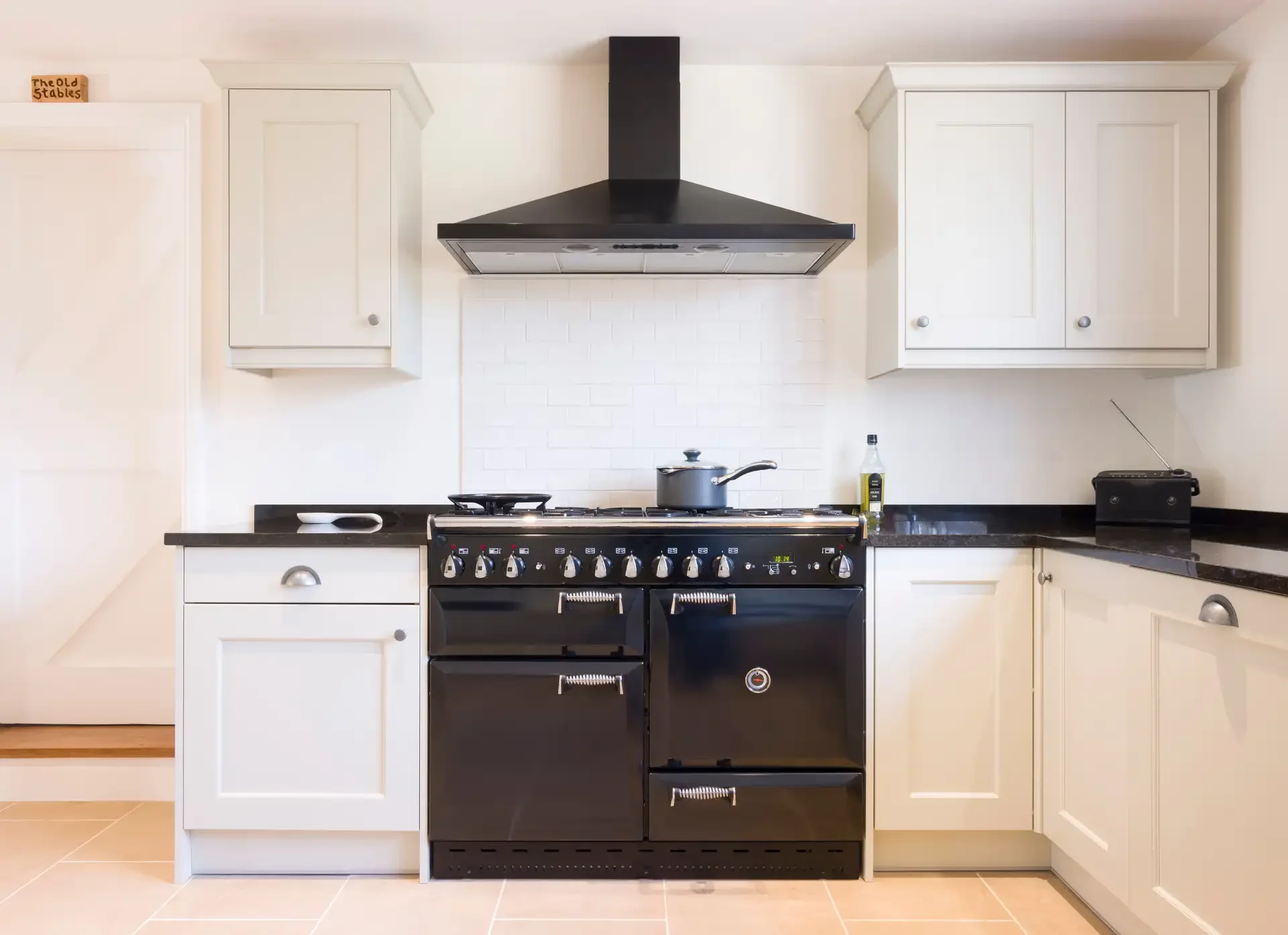 Black dual fuel range oven with multiple burners installed in modern white kitchen beneath stainless steel range hood