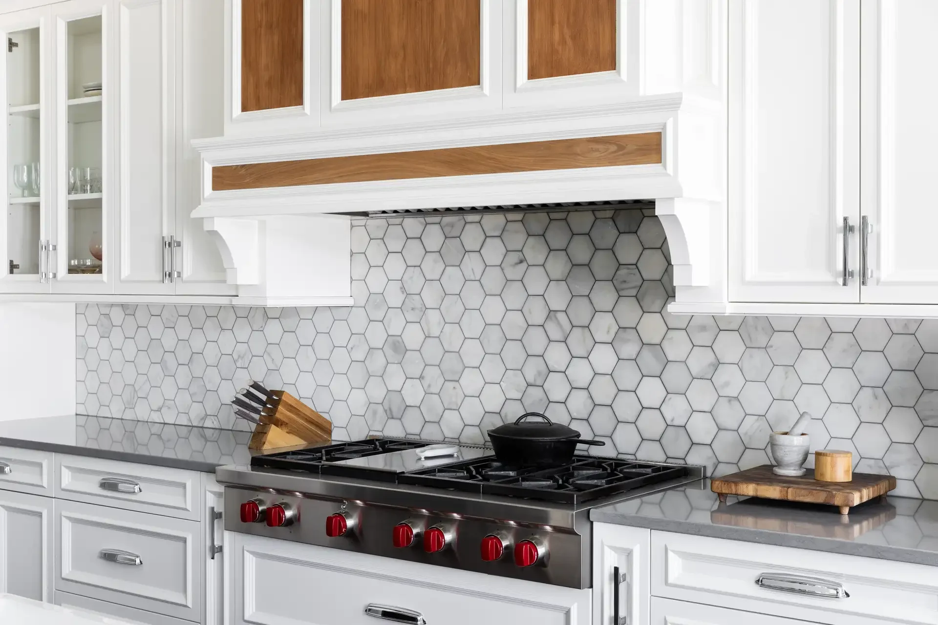 Modern kitchen with stainless steel gas range featuring red knobs, cast iron pot, and honeycomb tile backsplash