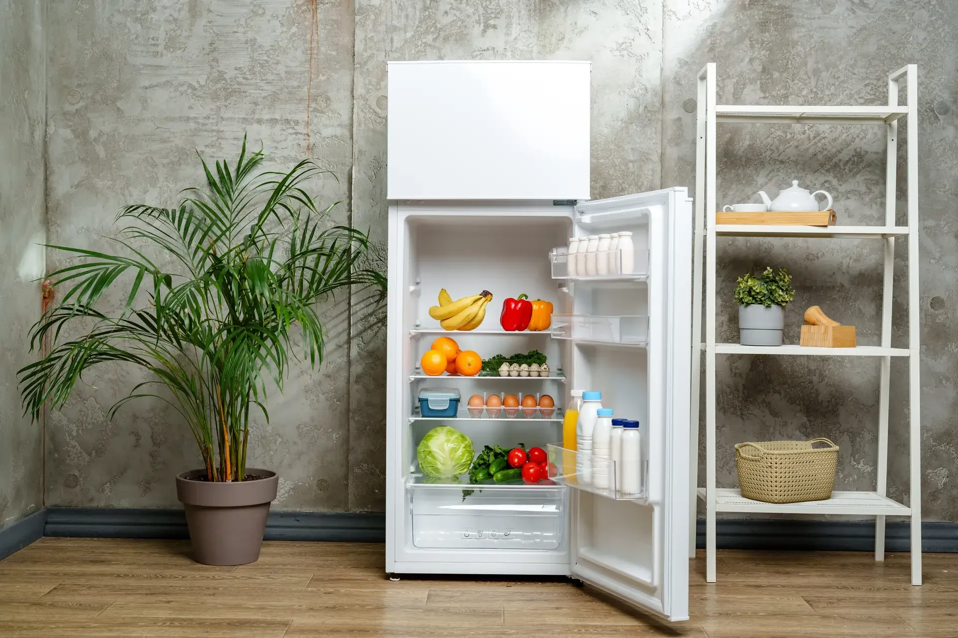 Open refrigerator door revealing fully stocked shelves with fresh fruits, vegetables, dairy products, and beverages in a clean kitchen setting