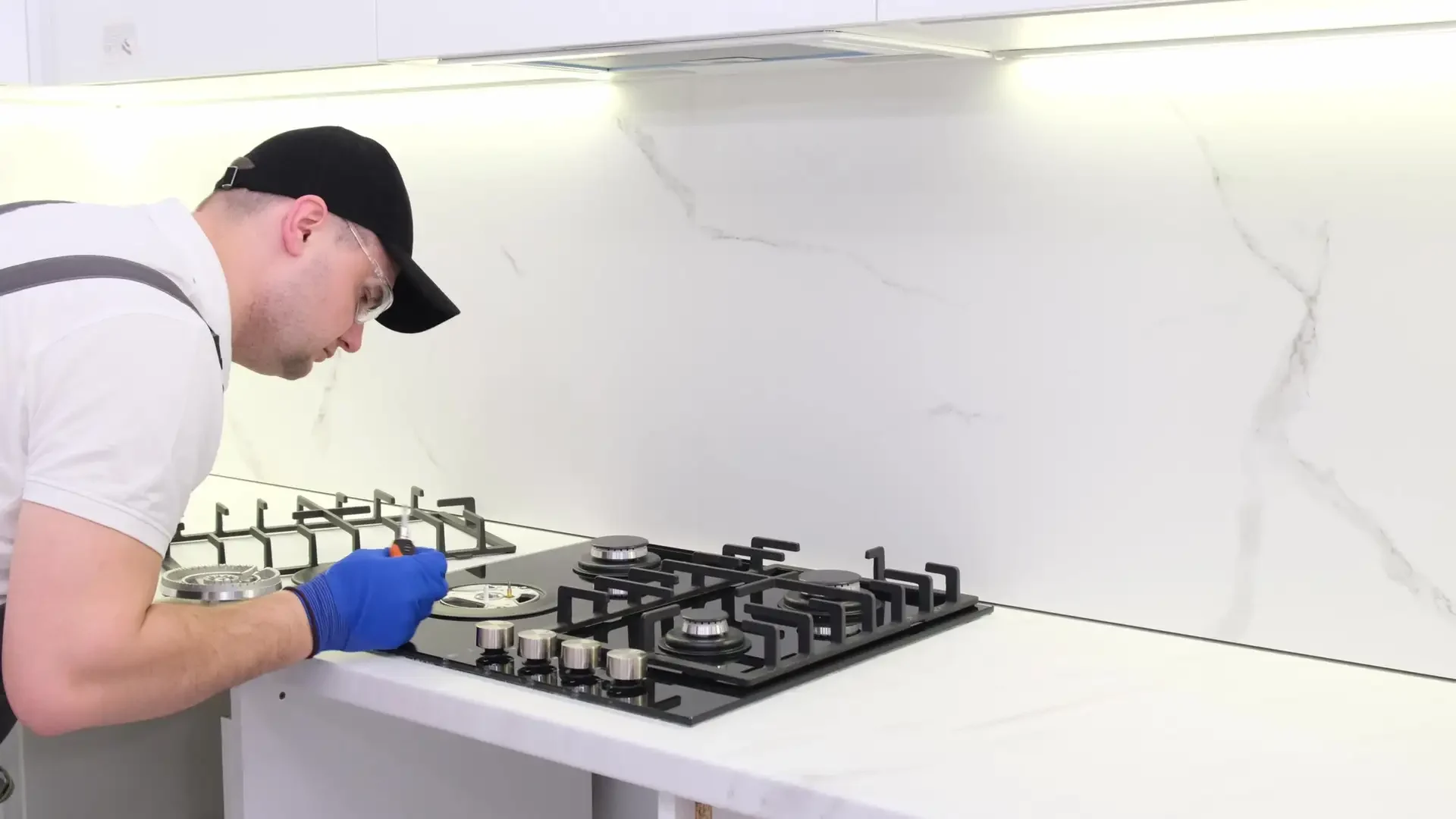 Professional technician wearing safety glasses and gloves repairs gas cooktop burner assembly using hand tool