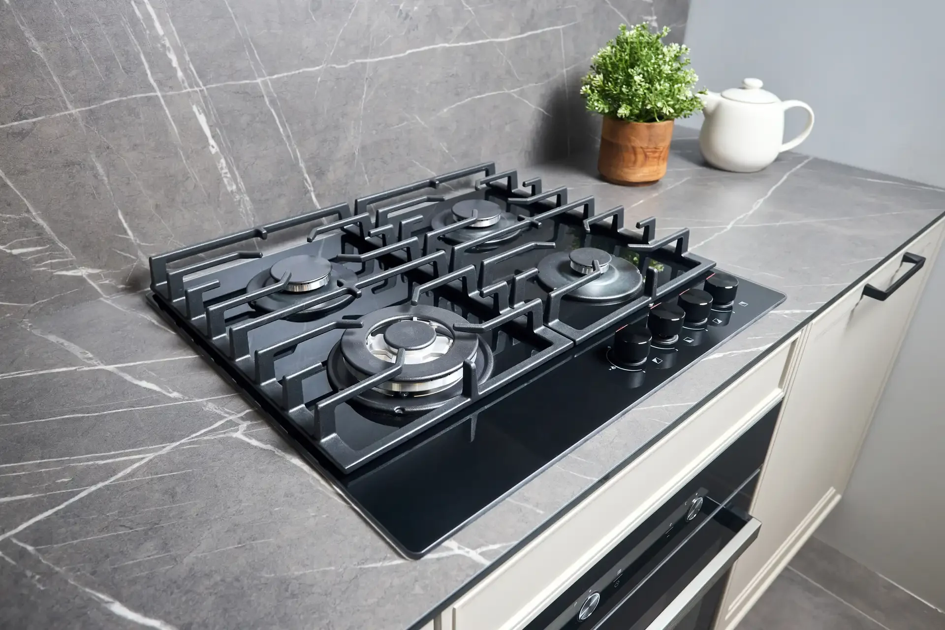 Modern gas stove with four burners and cast iron grates installed in upscale kitchen with grey stone countertop and backsplash