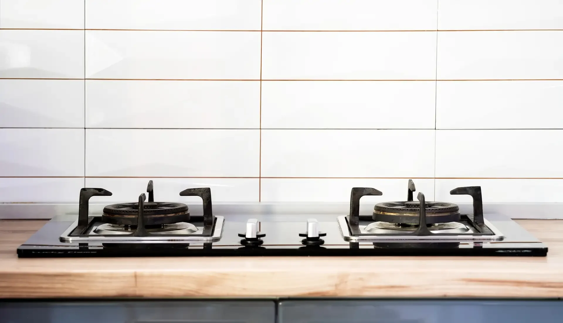 Modern two-burner gas cooktop installed on wooden kitchen counter with white tile backsplash, showing clean unused appliance in pristine condition