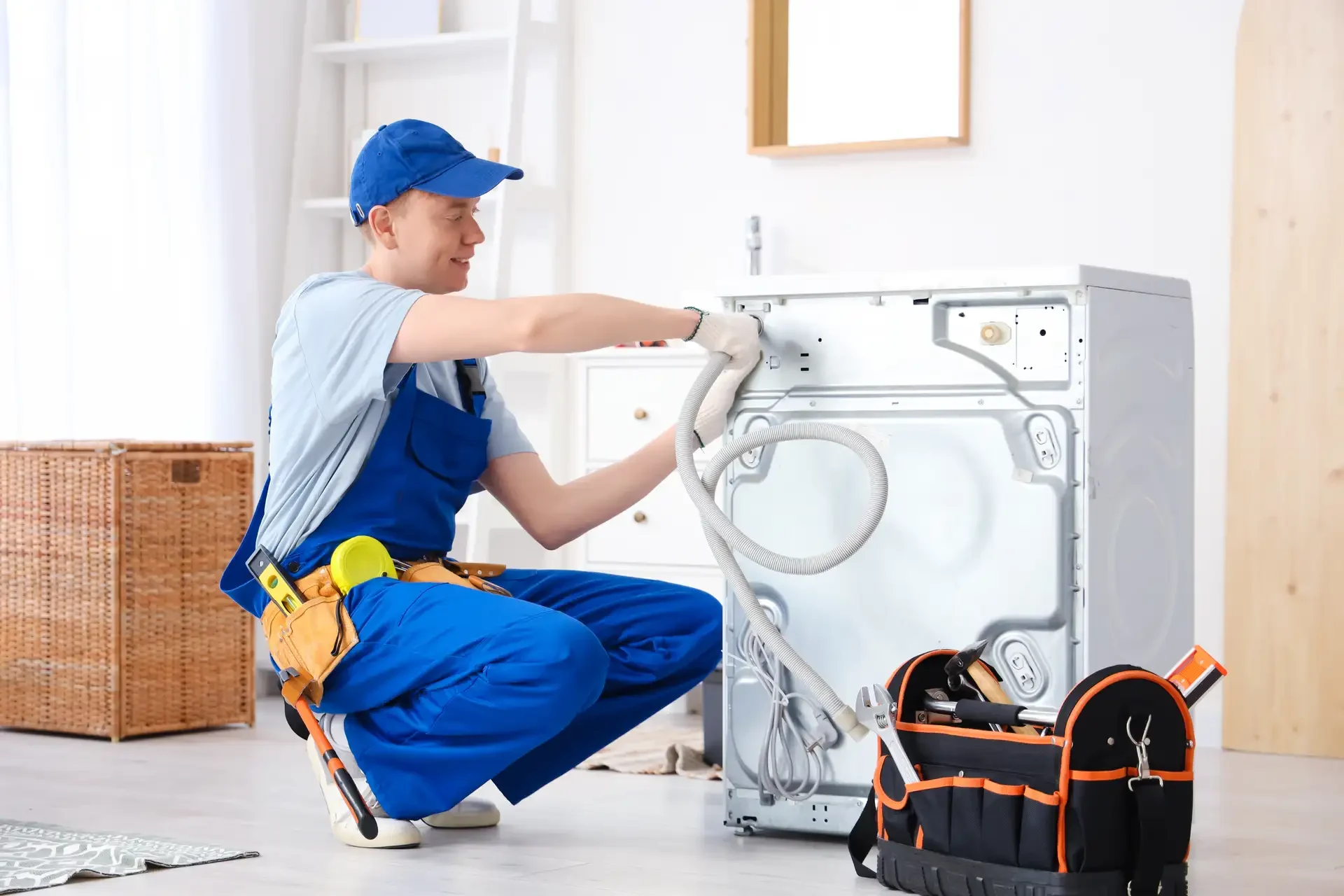 Professional technician in overalls adjusting water hoses and connections on the back of a washing machine during repair service