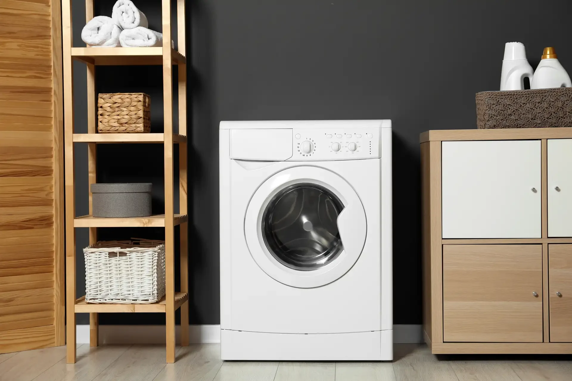 Front-loading washing machine in organized laundry room with wooden shelving and storage cabinet