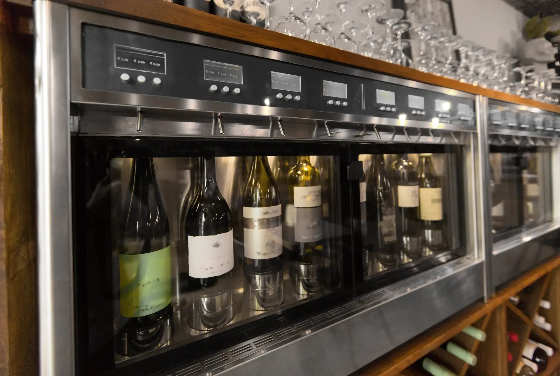 Refrigerated wine dispensing machine with multiple bottles behind glass panels, individual nozzles, and electronic controls in wine service area