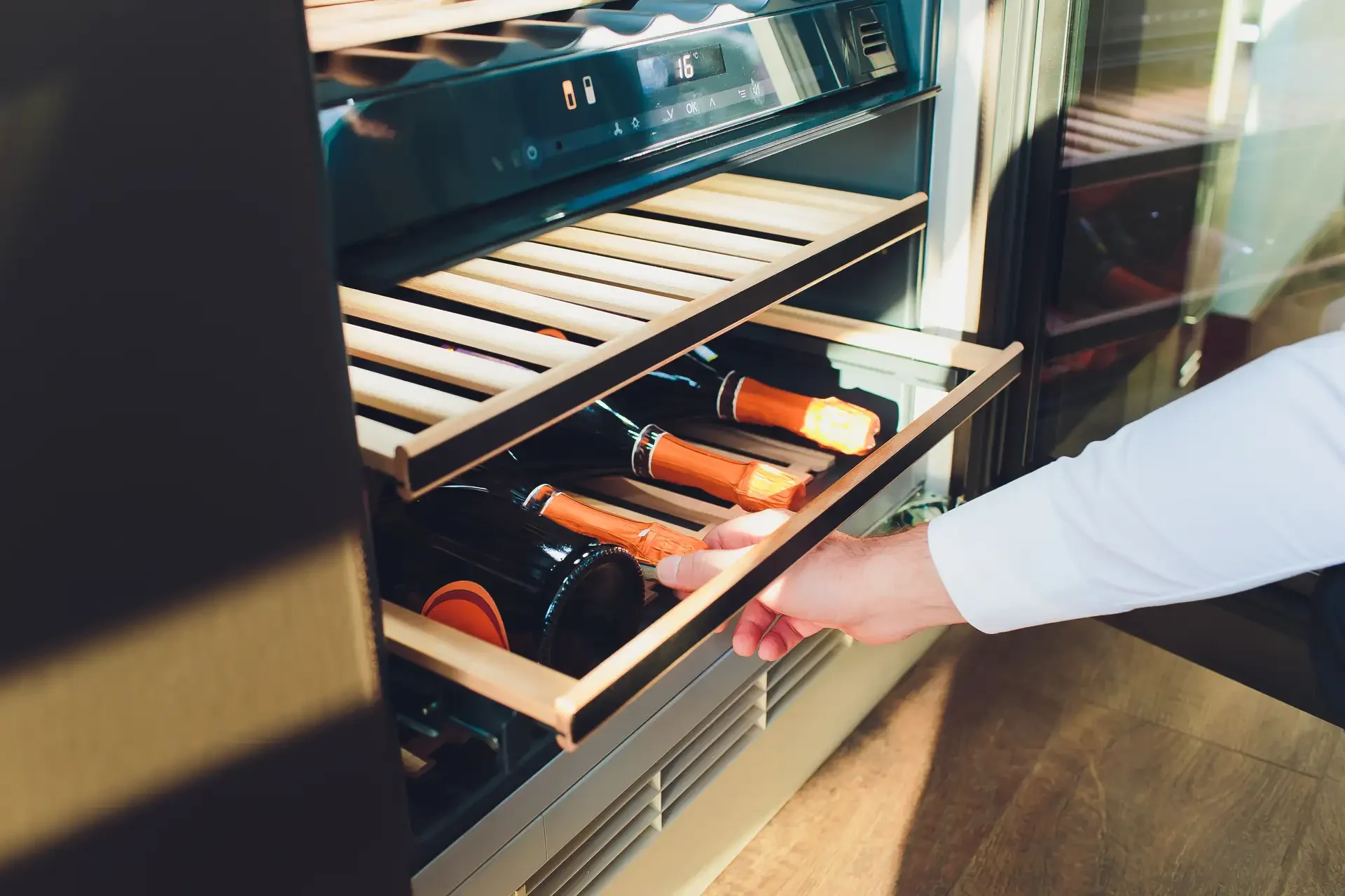 Person accessing built-in wine refrigerator with digital display and wooden racks storing multiple wine bottles